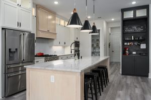 Modern kitchen with white cabinets, black pendant lights, marble island, gray hardwood floors and black chalkboard accent wall.