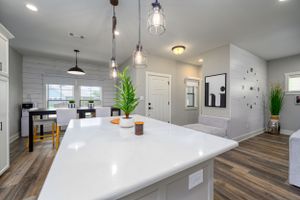 Modern open concept kitchen with white counters, pendant lights and hardwood floors.