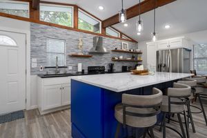 Modern kitchen renovation showcases white cabinetry, blue center island, pendant lighting and wood beam accents.