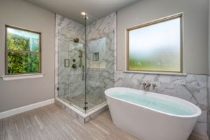 Luxurious master bathroom featuring freestanding tub, marble shower, and large windows with natural light.