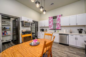 Bright eat-in kitchen with wooden table, white cabinets, and pink accent curtains.