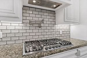 Modern kitchen with white subway tile backsplash, stainless steel gas cooktop, and granite countertops.