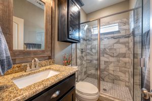 Modern bathroom interior with granite countertops, glass shower enclosure, and elegant fixtures with neutral color scheme.