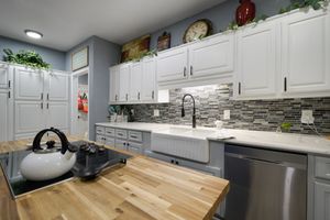 Modern white kitchen with butcher block island, mosaic backsplash, and stainless steel appliances in gray and white color scheme.