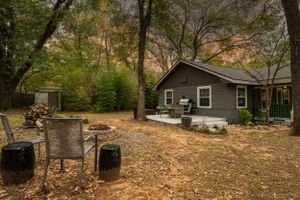 Cozy grey cottage in wooded setting with rustic outdoor cooking area.
