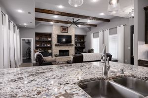Modern open concept basement renovation features granite countertops and exposed wood ceiling beams in neutral colors.