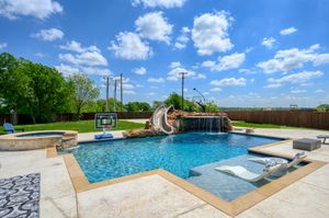 Luxurious backyard swimming pool with curved water slide, spa and travertine deck on a beautiful sunny day with blue skies.