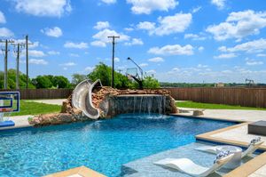 Swimming pool with rock waterfall feature and tanning ledge under bright blue sky.