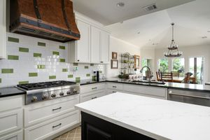 Modern white kitchen with copper range hood, marble countertops, and custom cabinetry.
