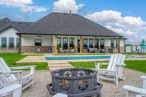 Luxurious backyard with swimming pool, Adirondack chairs, and decorative fire pit against modern home with covered patio.