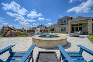 Backyard patio featuring stone hot tub, fire pit, and blue Adirondack chairs.