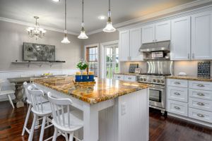 Bright white kitchen featuring pendant lights, granite countertops, and classic cabinetry with modern appliances.