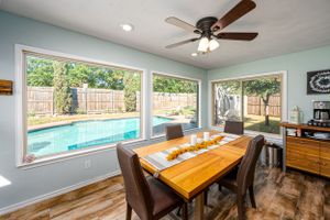 Bright dining area with wooden table overlooking backyard pool through large windows.