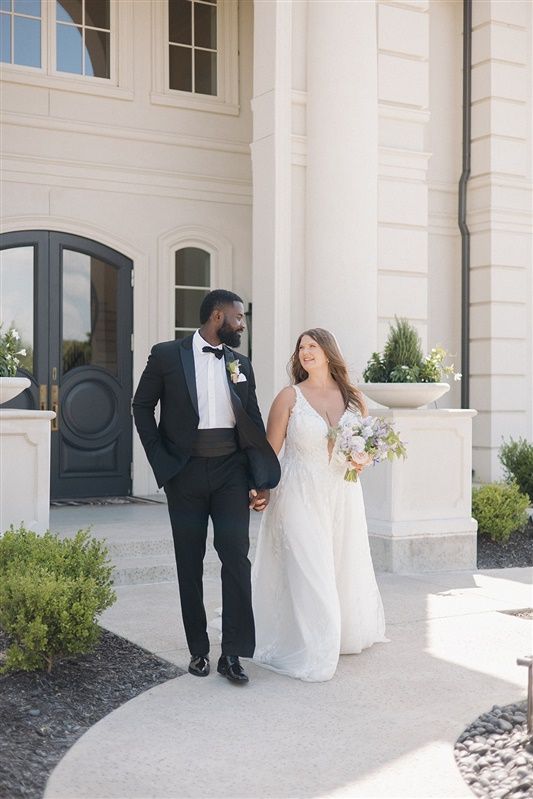 A bride and groom hold hands while walking outside an elegant white building with classical architecture and columns.