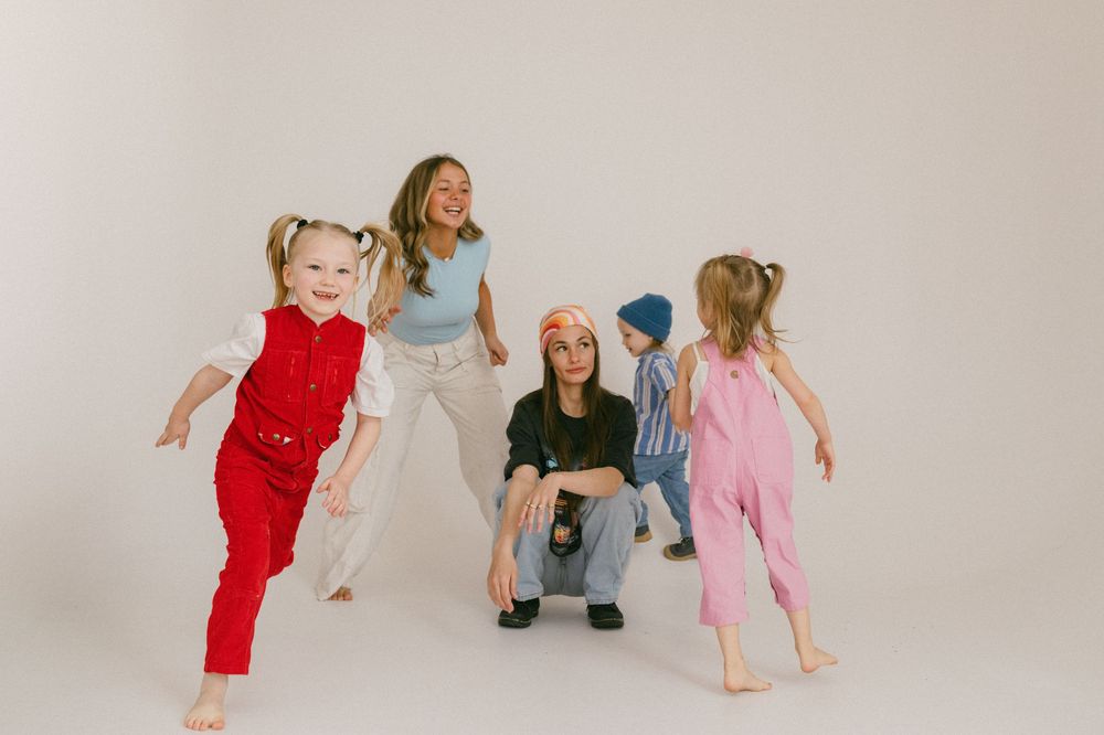 Energetic children in colorful jumpsuits dance and play on a white studio backdrop.