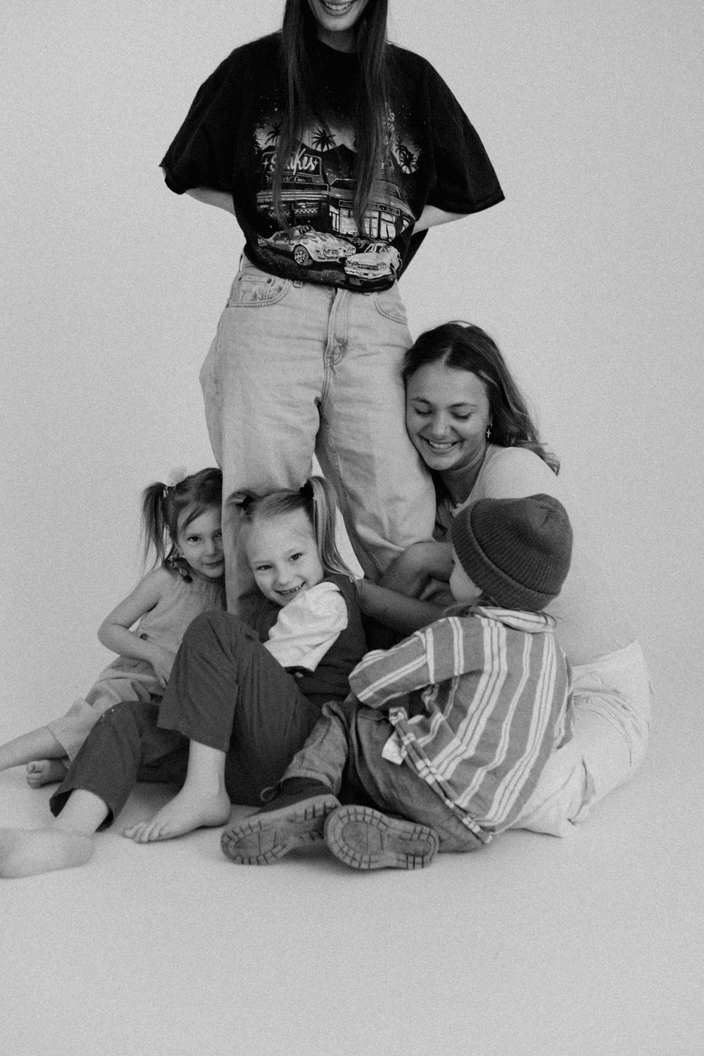 Black and white photo capturing a playful moment of people laying and sitting together against a white backdrop.