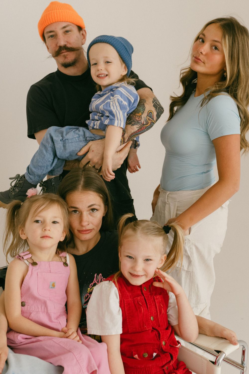 Portrait of family group wearing casual clothing with bright beanies and overalls posing against a white background.