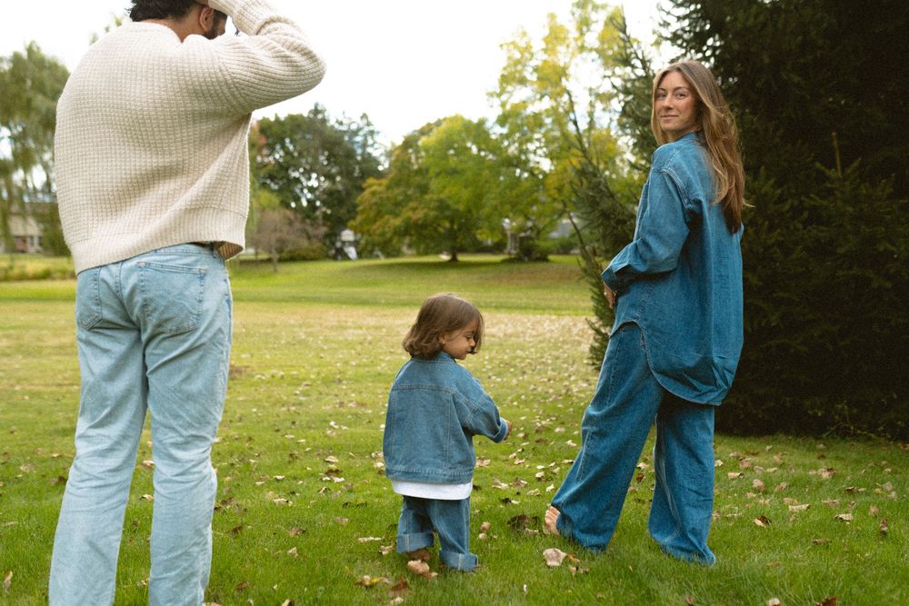 A photographer takes a picture of two people in matching blue outfits standing on grass in a park setting.
