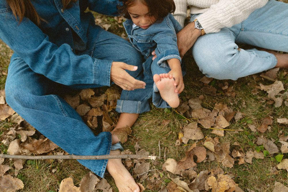 A person wearing denim crouches down to collect fallen autumn leaves from the ground.