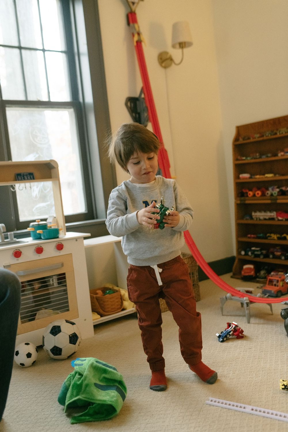 A playroom setting with toys scattered about including soccer balls and a red track, with natural light coming through a window.