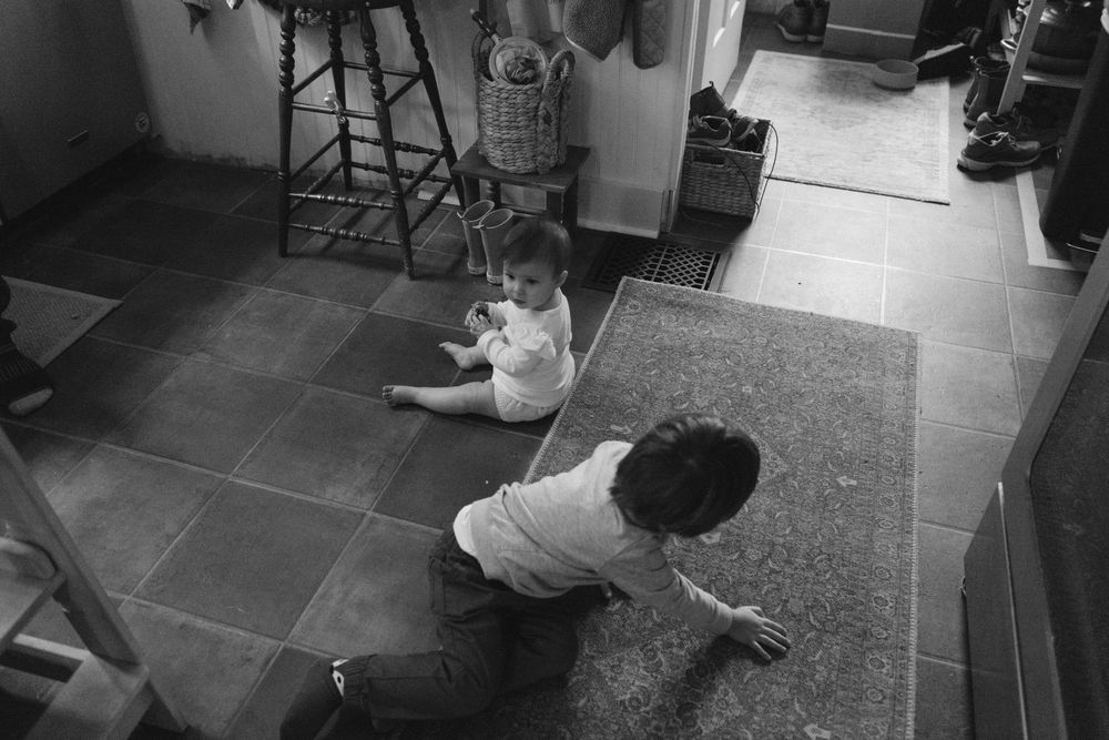 High angle black and white view of two people sitting and playing together on tile floor.