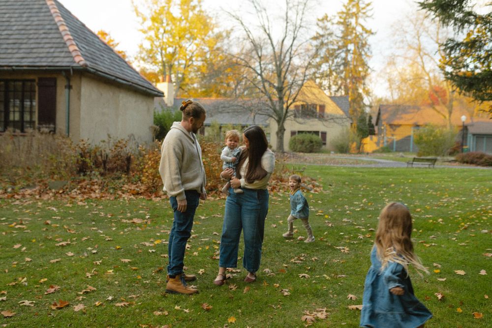 Children playing in a backyard during autumn with fallen leaves scattered on the grass.