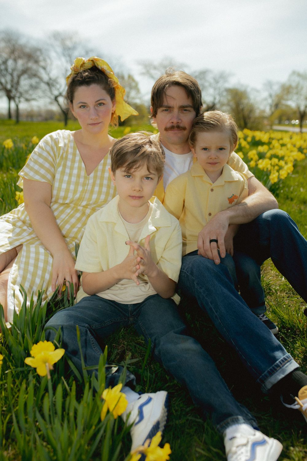 A family sits together in a sunny spring field surrounded by blooming yellow daffodils.