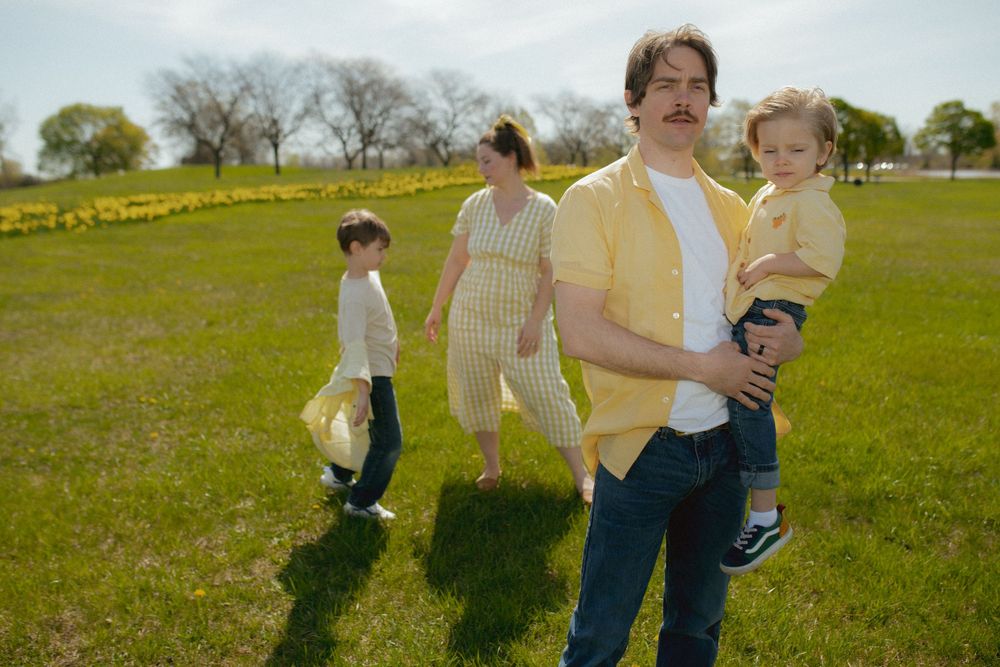 Family group walking together in spring meadow filled with yellow flowers on sunny day.