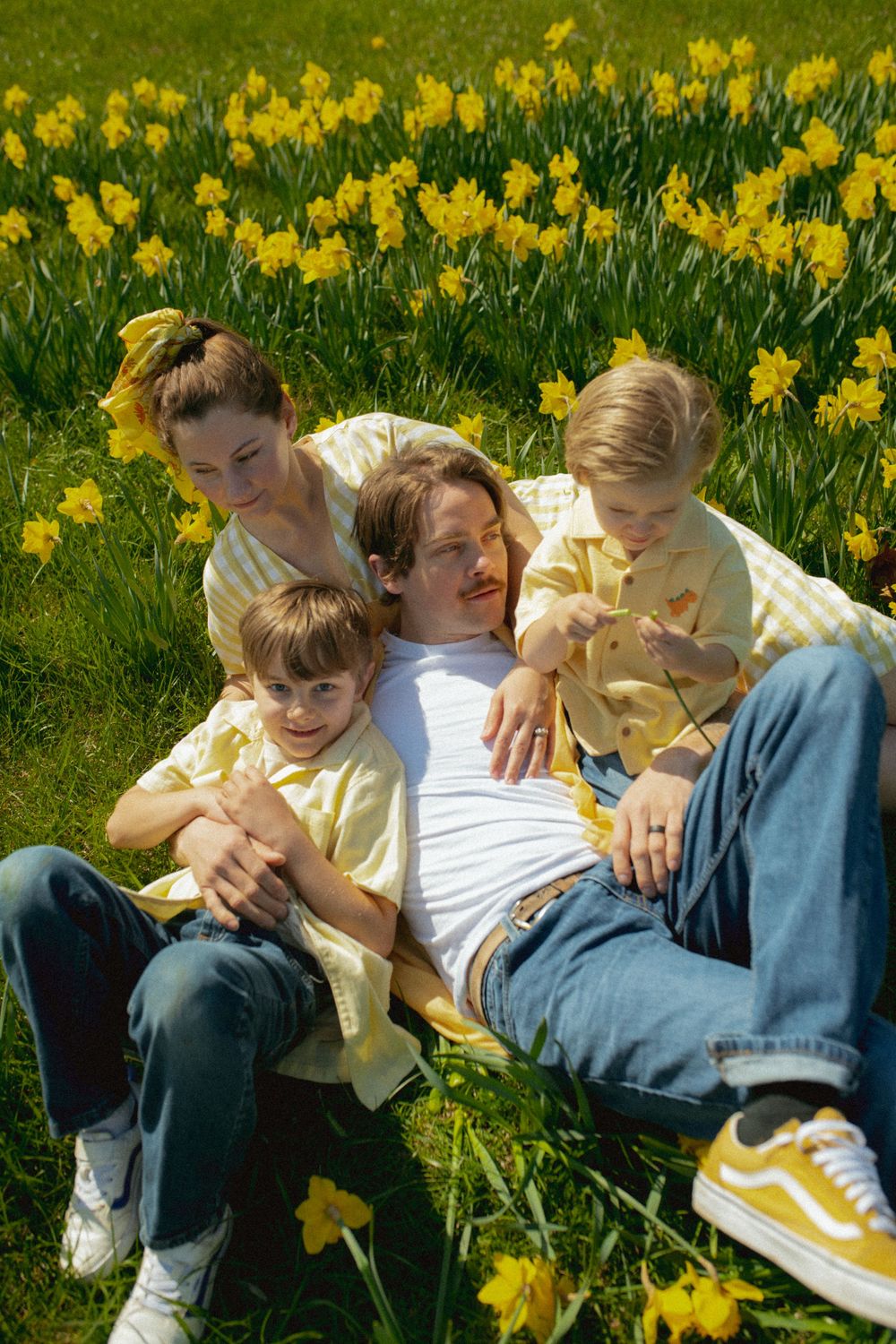 A group relaxes together on green grass surrounded by blooming yellow daffodils on a sunny spring day.