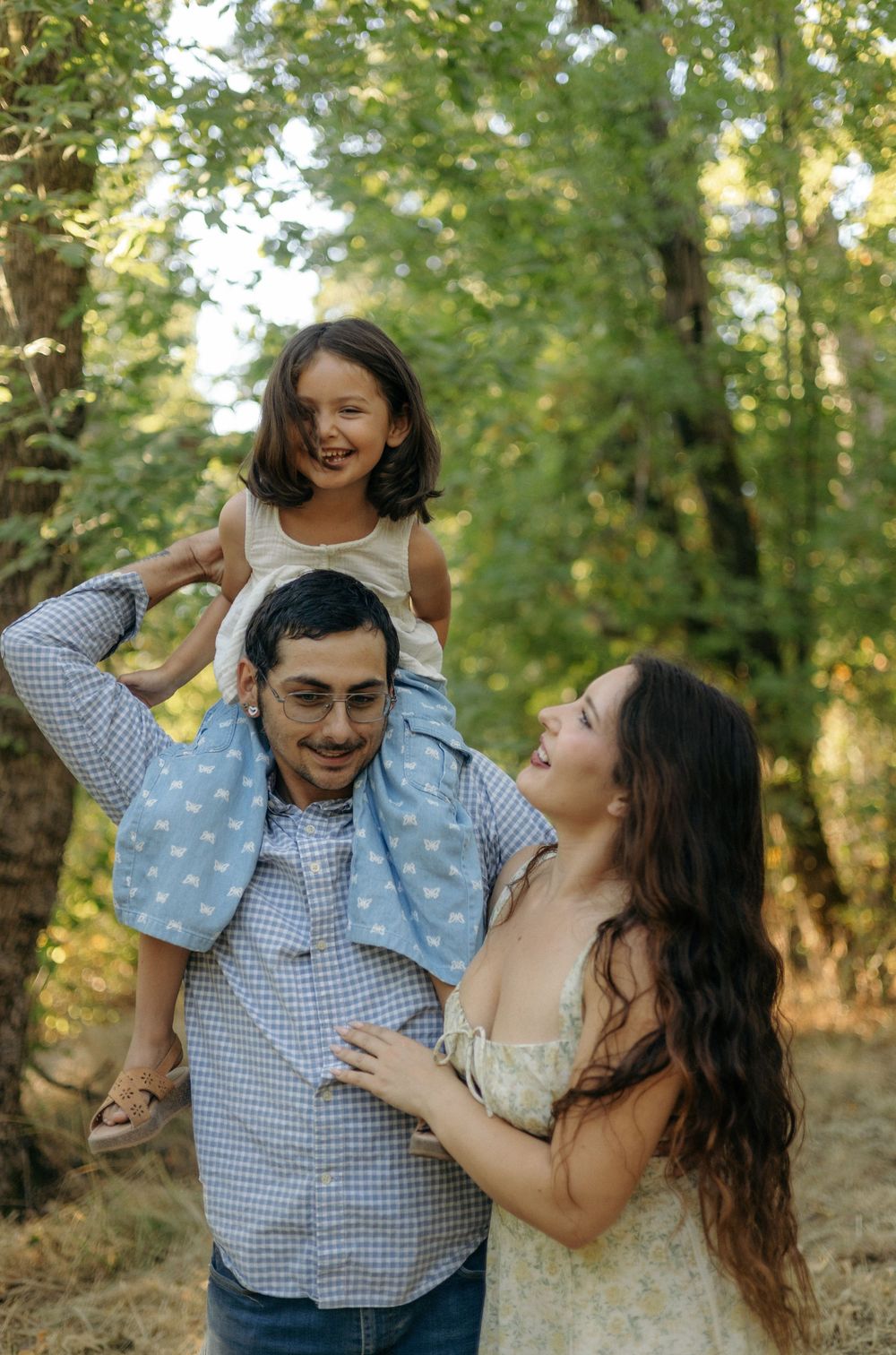 A joyful couple shares playful moments together while posing for a series of photos in a sunlit forest setting.