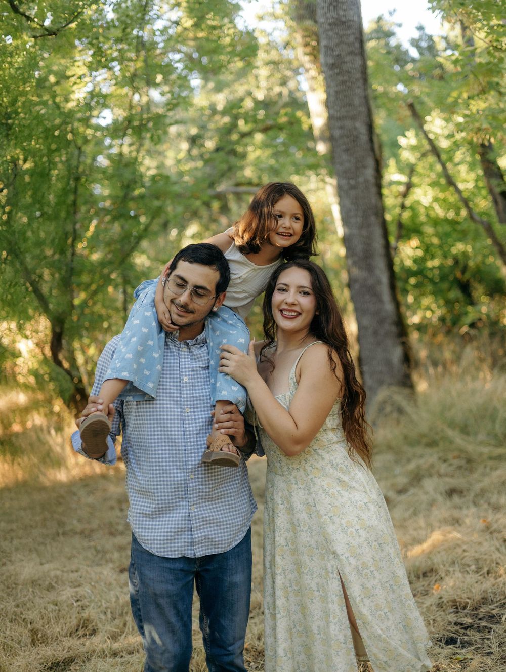 A couple shares joyful laughter together during an outdoor photoshoot in a sunlit wooded setting.