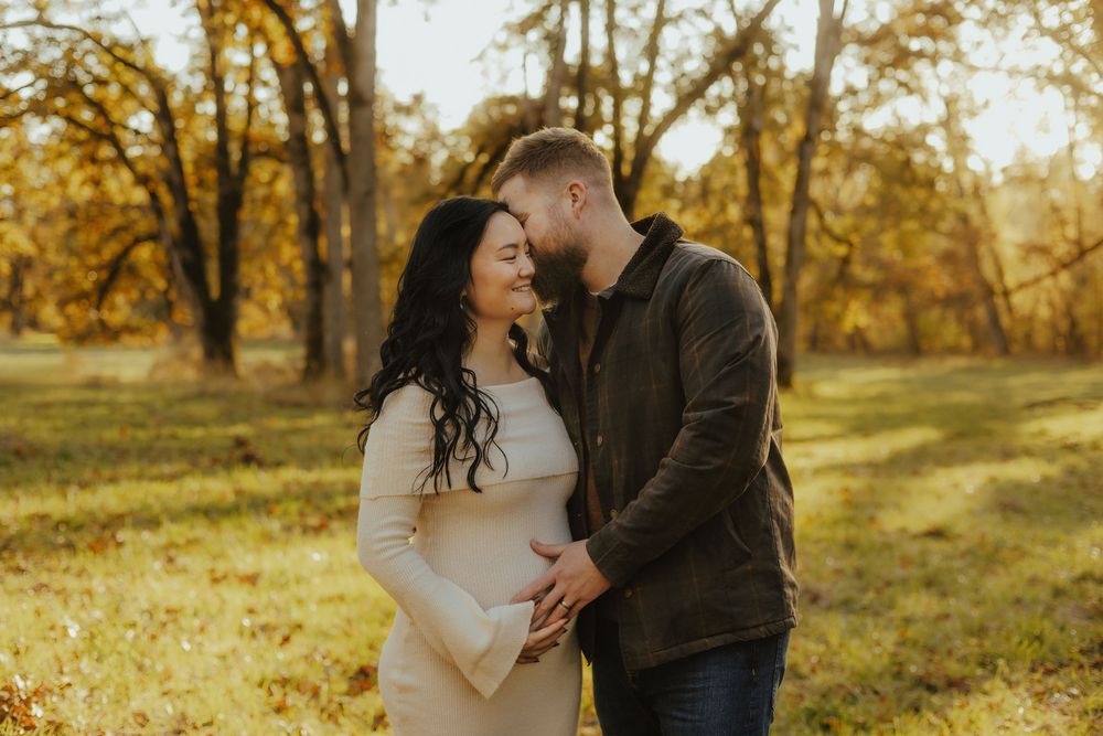 A couple shares tender moments in a golden autumn forest setting during a romantic outdoor photoshoot.