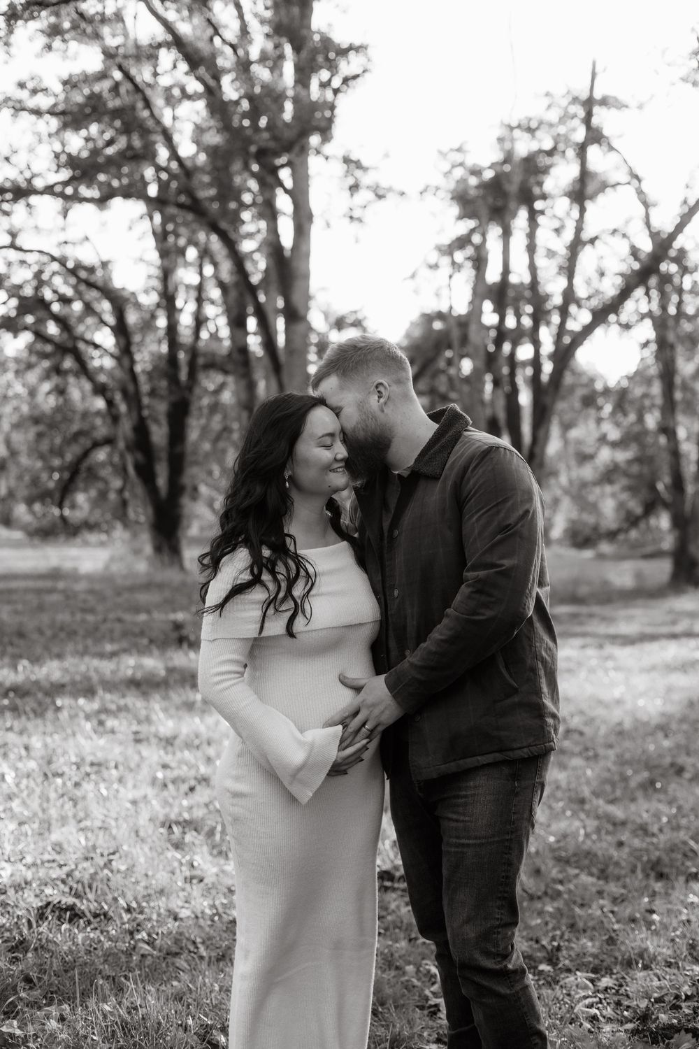 A romantic black and white photo series of a couple sharing tender moments in a wooded outdoor setting.