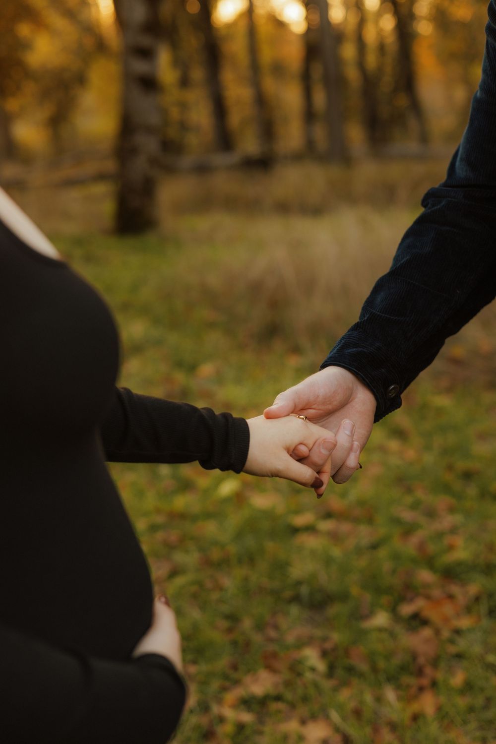 Two people hold hands against an autumn forest background with golden sunlight filtering through the trees.