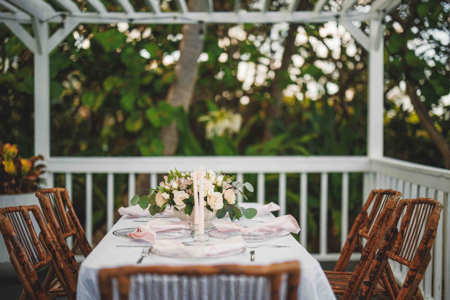 An elegant outdoor table setting on a white porch with wooden chairs.
