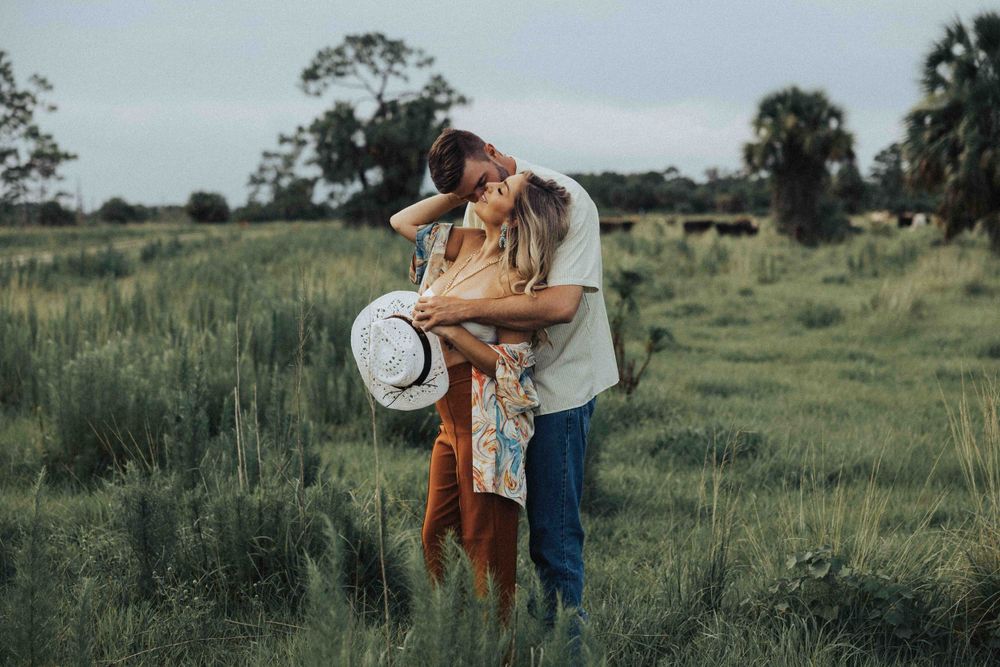 A romantic embrace in a rustic field with palm trees and natural scenery.