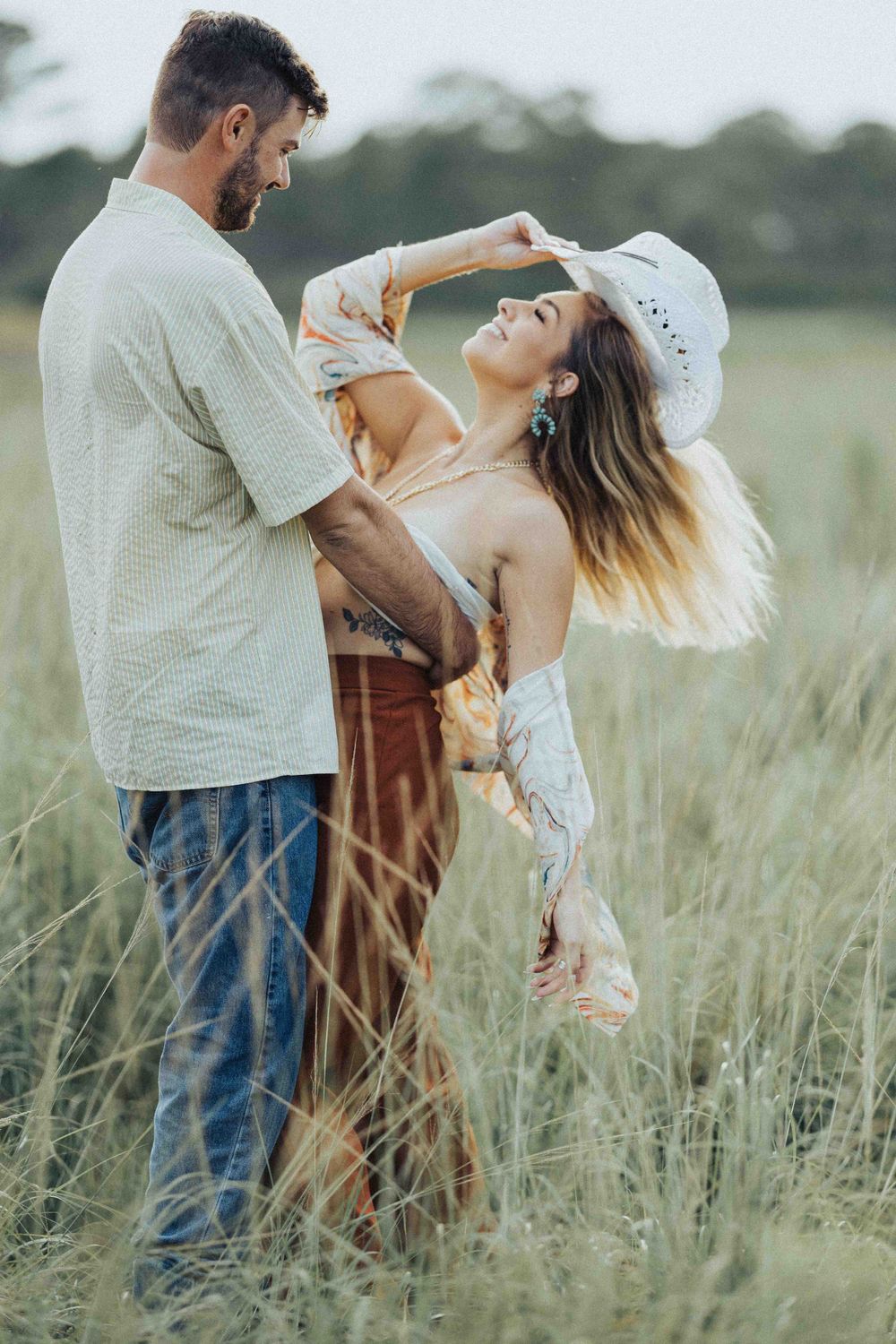 A romantic couple dances together in tall grass during golden hour.