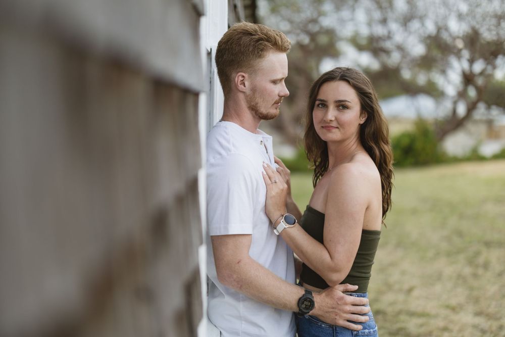 A couple shares an intimate moment against a white wall in an outdoor setting.