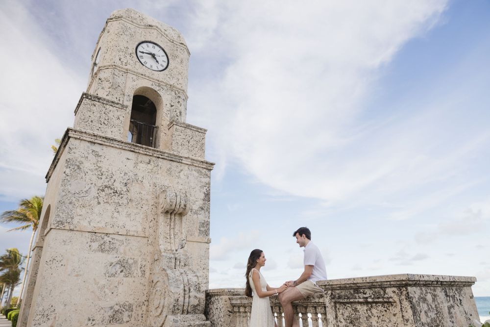 A romantic moment captured near a historic clock tower under cloudy skies.