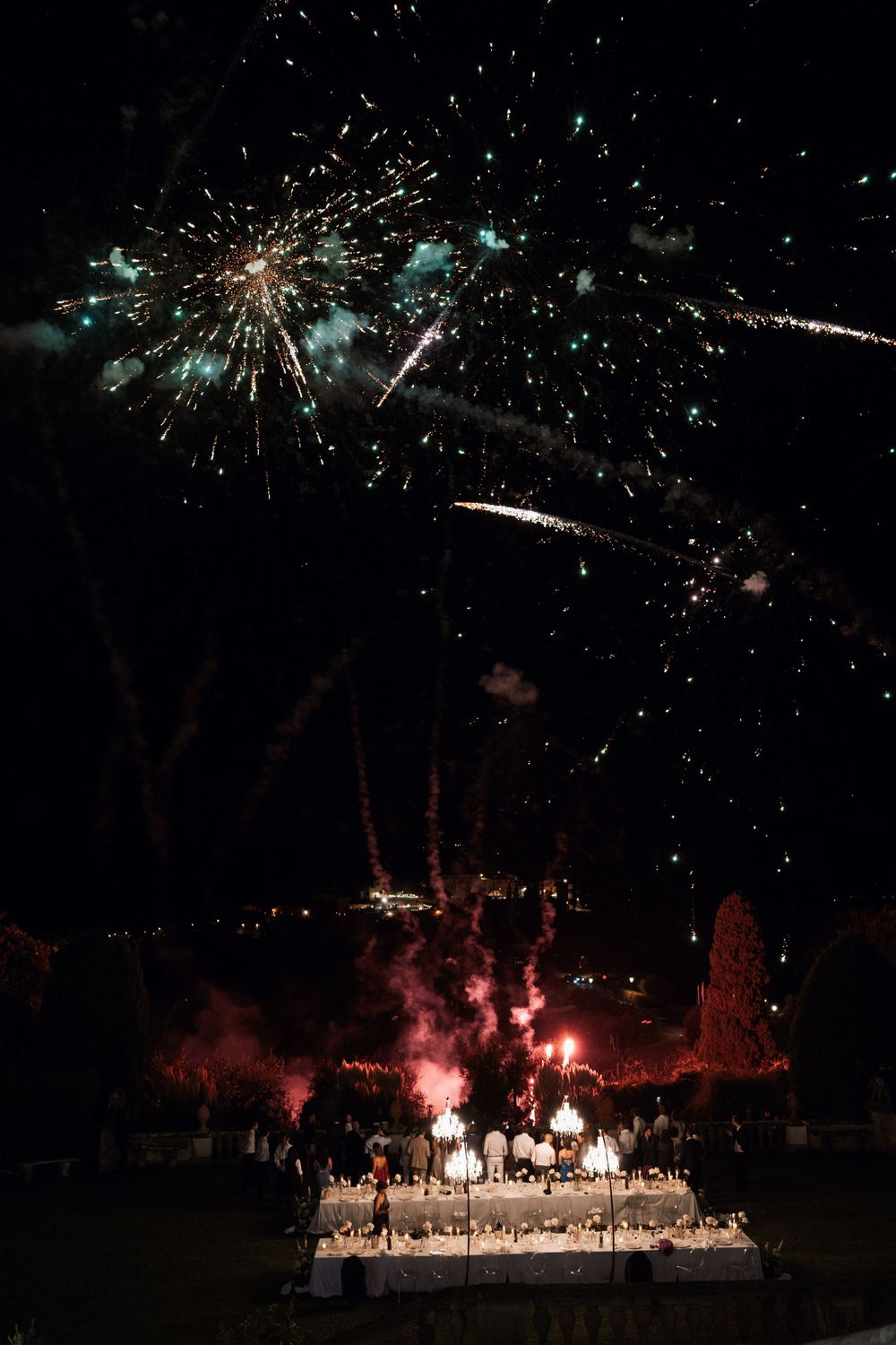 Fireworks display illuminating the night sky above an elegantly decorated outdoor wedding table in Tuscany