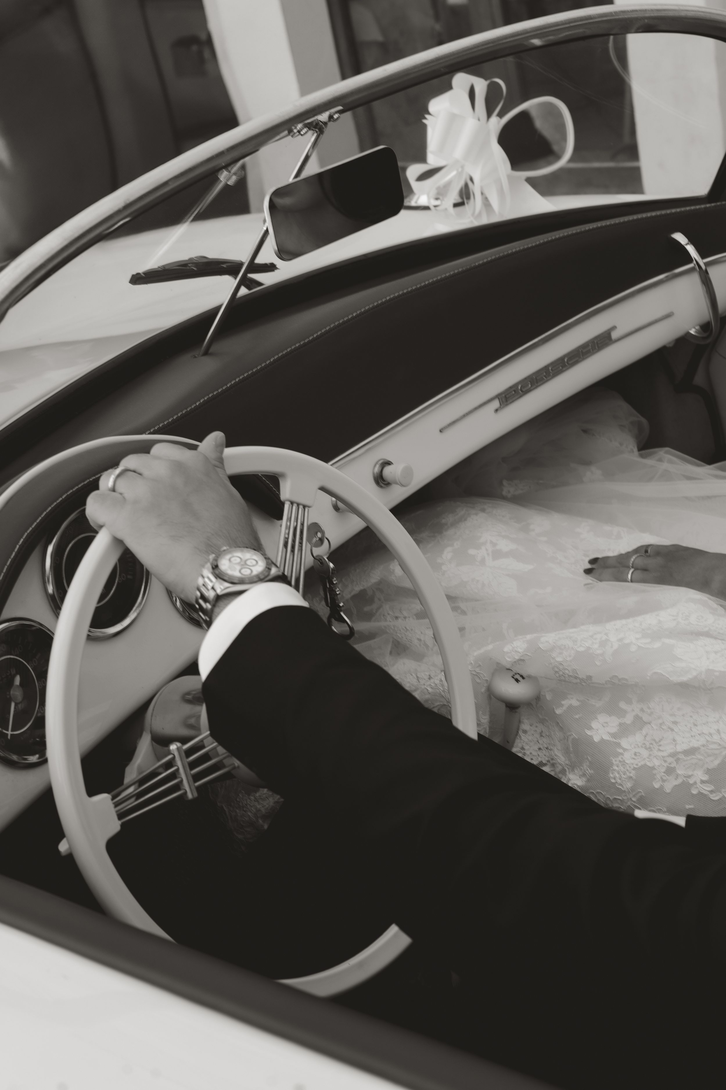 Black and white image showing hands on a vintage car steering wheel with a view of the dashboard interior.