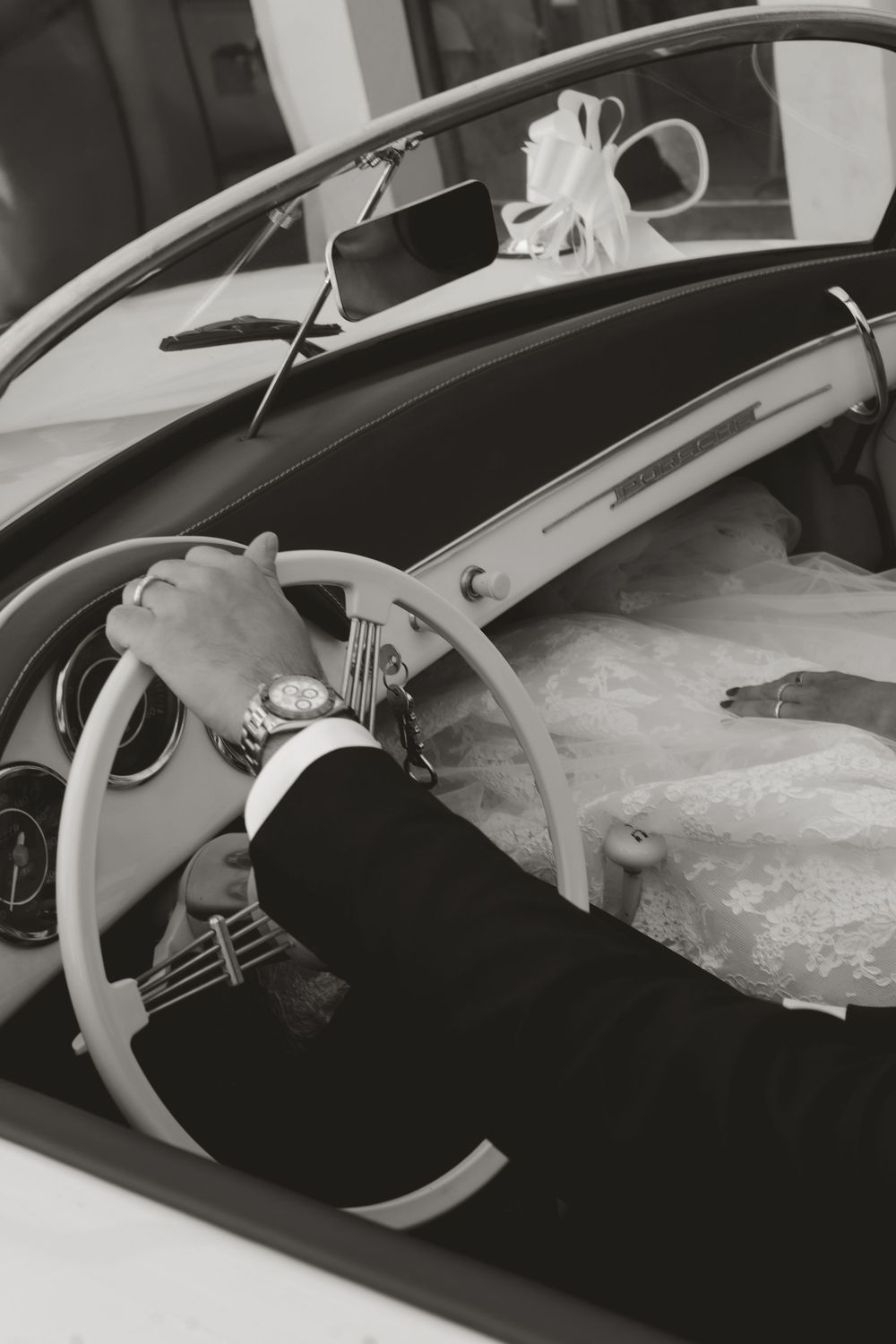 Black and white image showing hands on a vintage car steering wheel with a view of the dashboard interior.