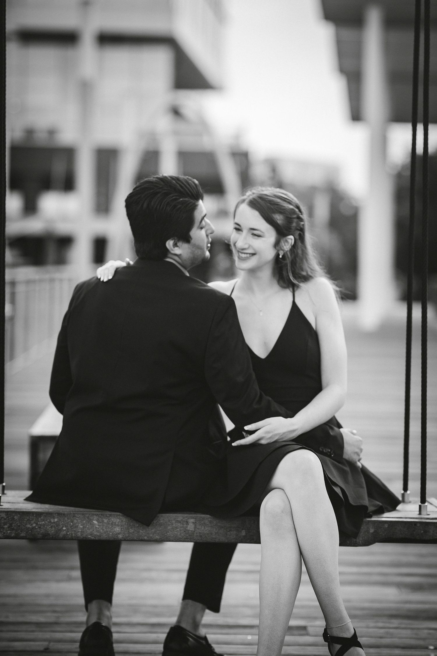 A romantic black and white photo showing a couple sitting together on a bench at the Wharf in Washington DC