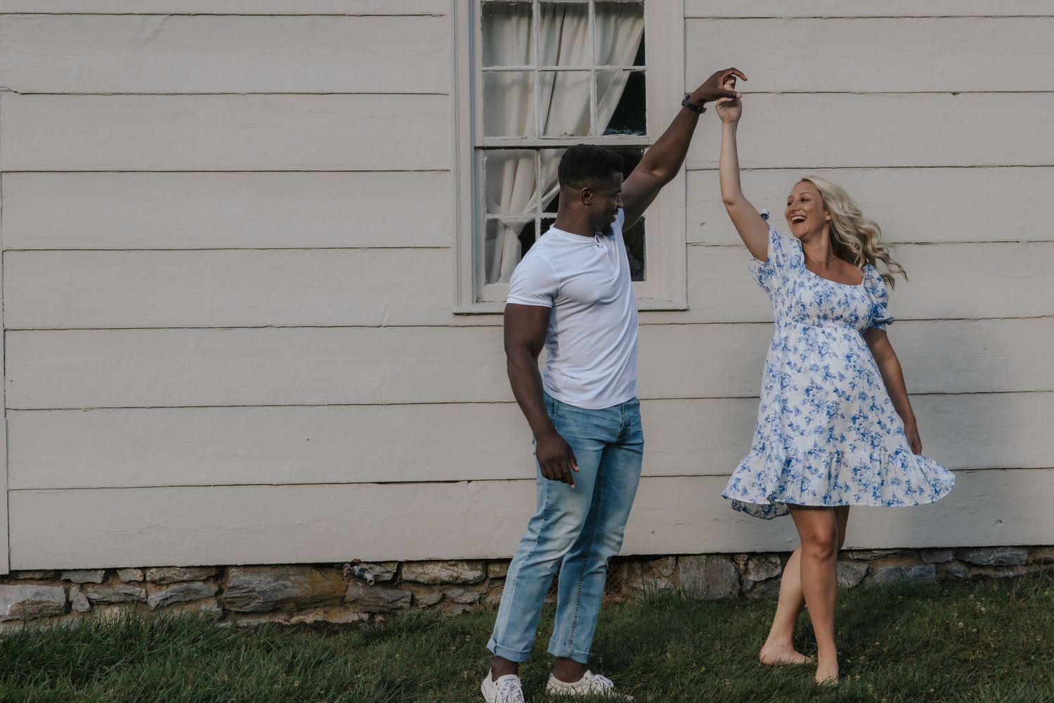Couple dancing together outside white house during sunset photoshoot.
