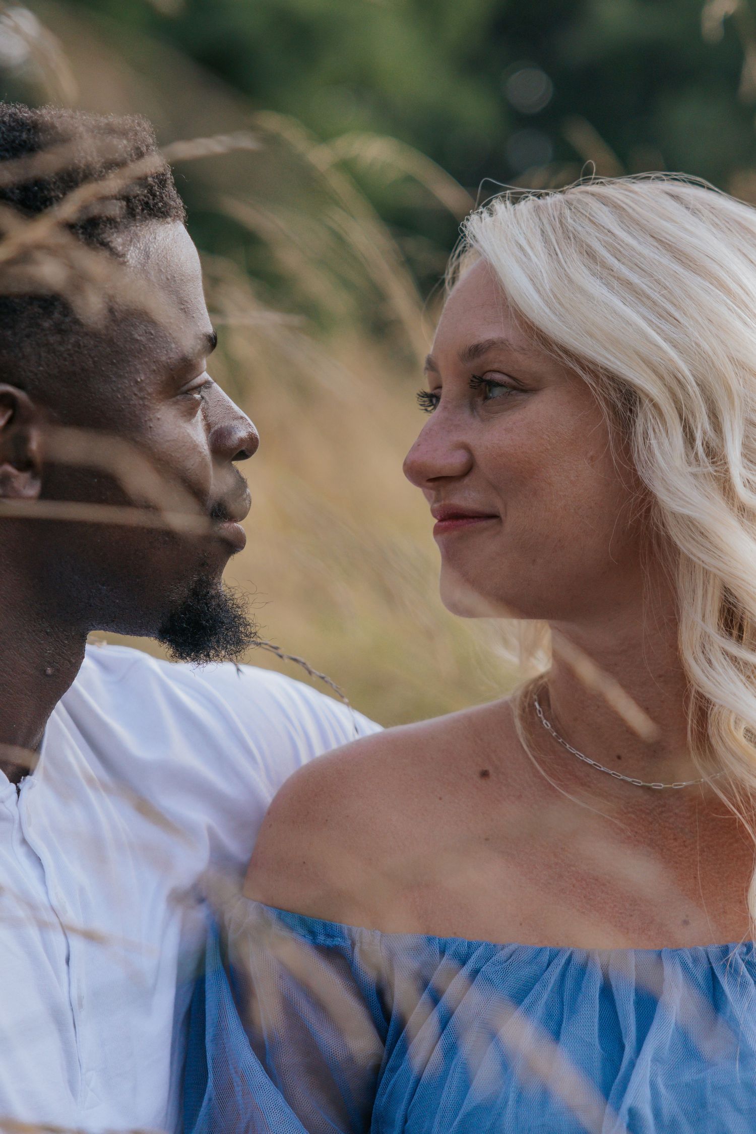 Intimate close-up portrait of couple among tall grass at sunset.