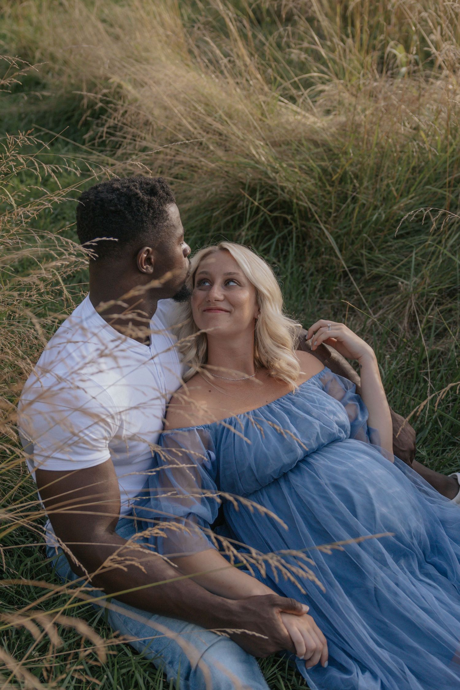 Couple relaxing together in tall grass during golden hour photoshoot.