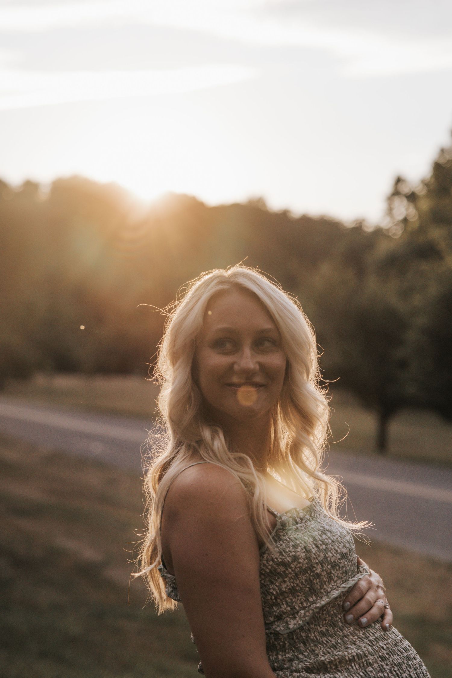 Maternity portrait at sunset with woman in sparkly dress smiling over her shoulder.