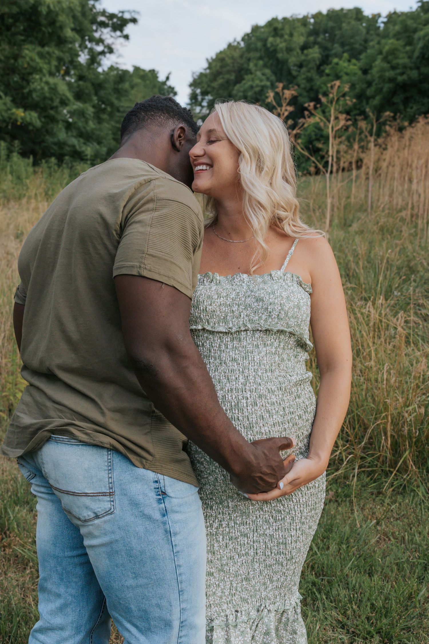 Intimate outdoor maternity photo of couple sharing tender moment in field of tall grass.