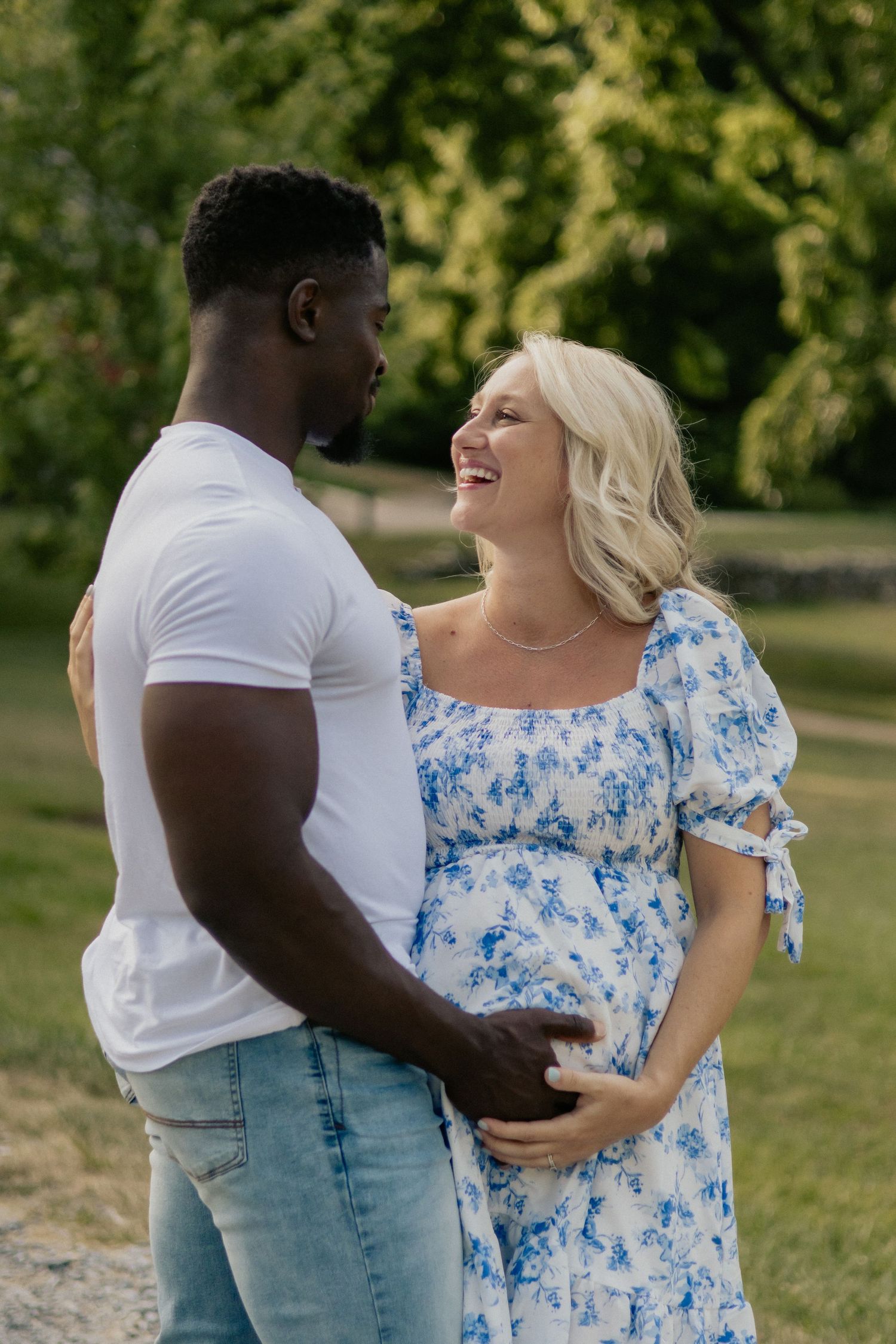 Joyful outdoor maternity session with couple in casual attire sharing loving moment.