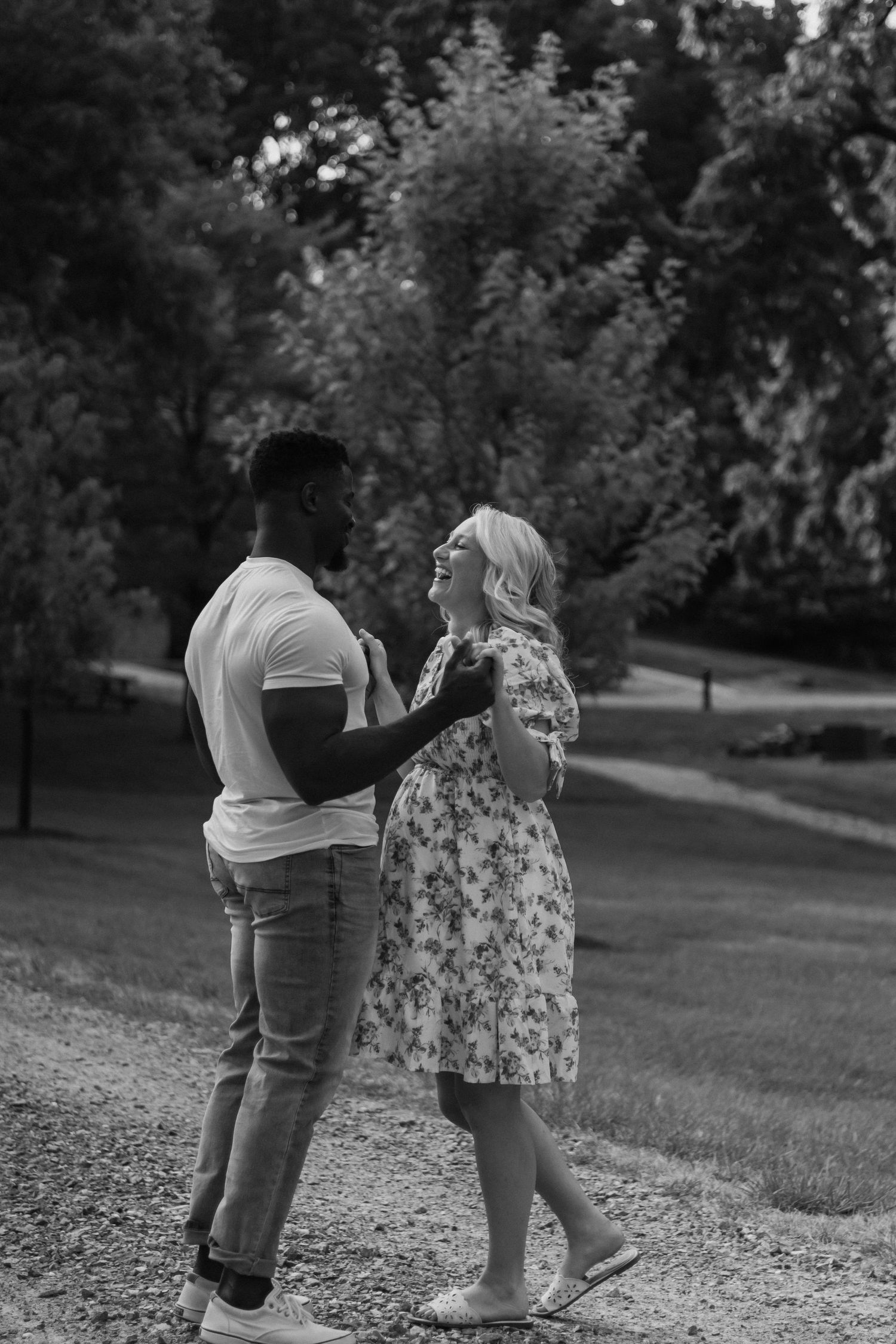 A couple dances together on a path surrounded by green trees in a black and white photo.